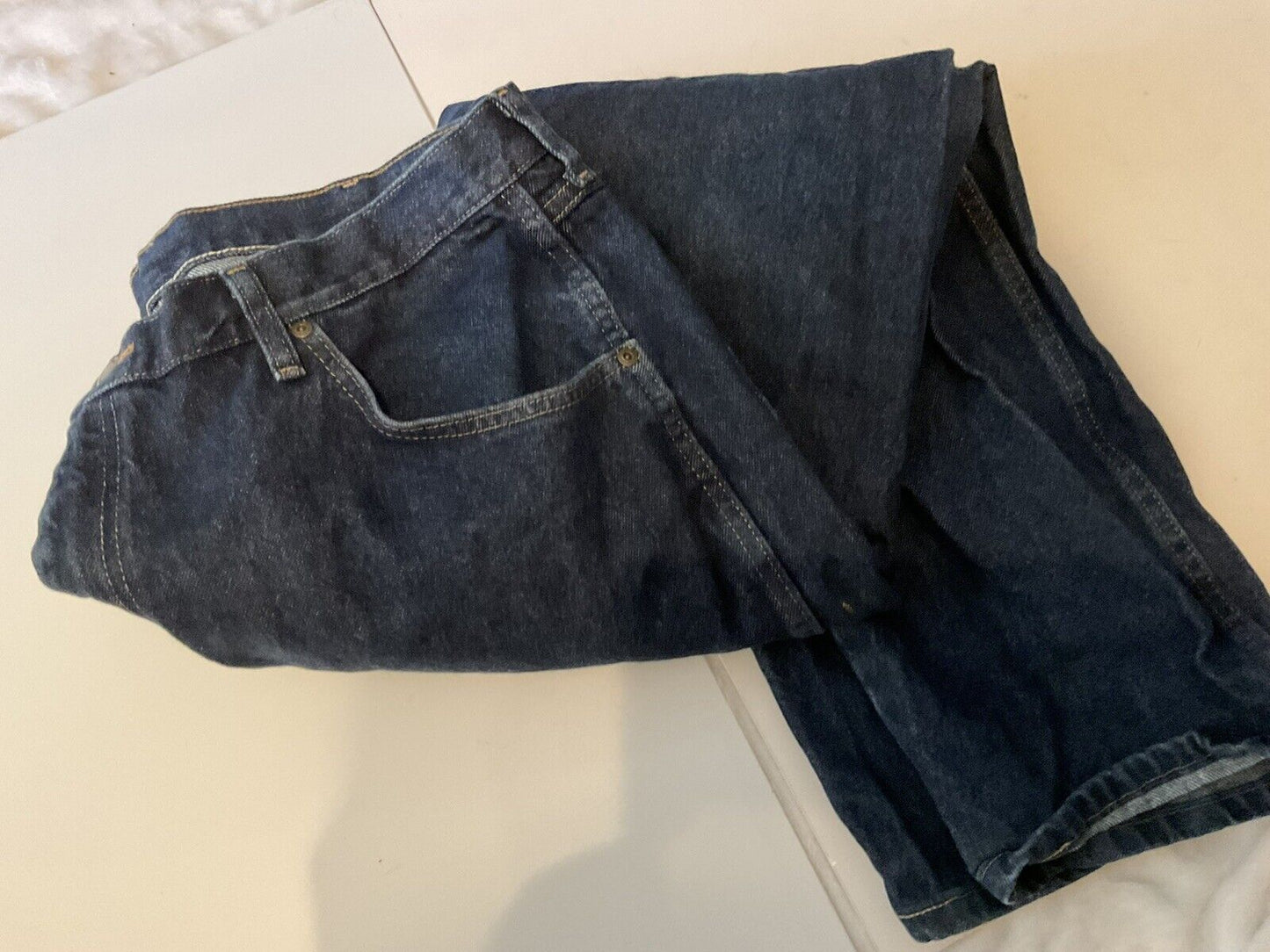 Wrangler relaxed fit jeans men folded dark blue denim with front pocket belt loops on white surface