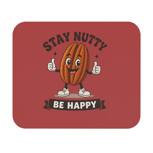 A square product with rounded corners, likely a mouse pad or desk mat, featuring a cartoon smiling walnut character giving two thumbs up. The background of the product is a dusty brick red, with the text 'STAY NUTTY BE HAPPY' printed in dark brown and white.