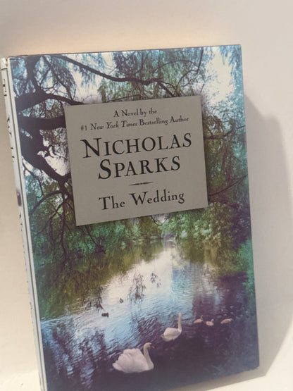 Hardcover book titled The Wedding by Nicholas Sparks, placed on a rustic wooden table with soft lighting, emphasizing its romantic theme.