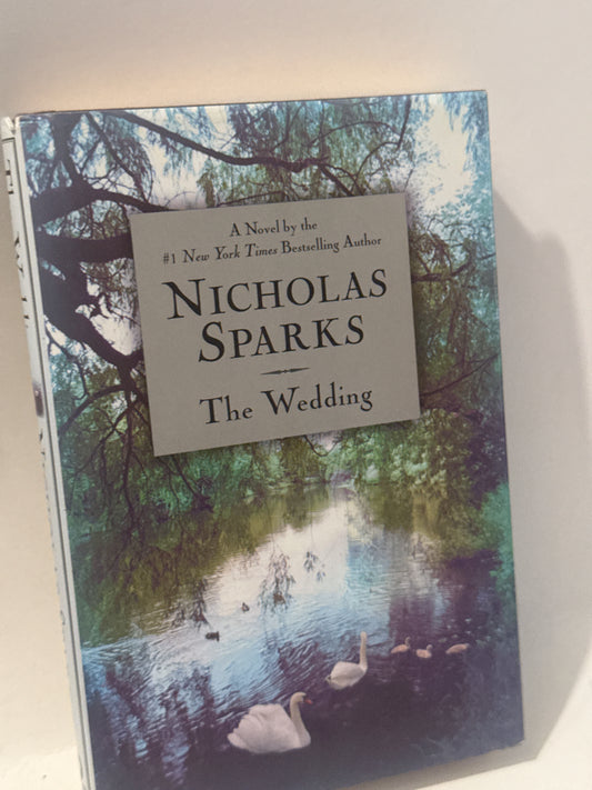 Hardcover book titled The Wedding by Nicholas Sparks, placed on a rustic wooden table with soft lighting, emphasizing its romantic theme.