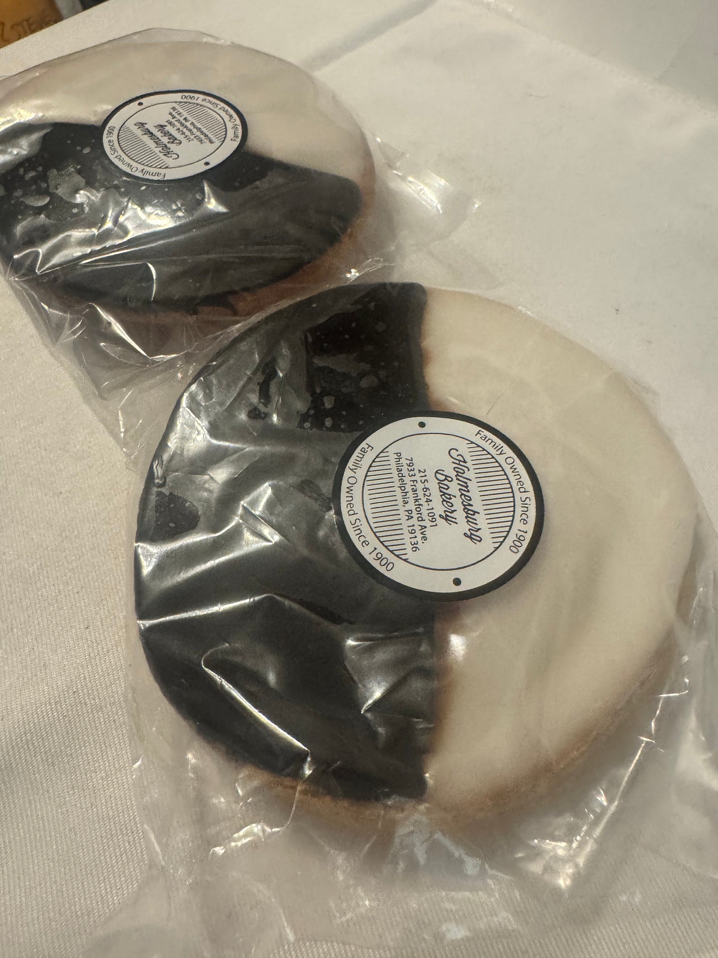 Two round frosted pastries, one chocolate chip and one chocolate chip cookie, individually wrapped in clear plastic with a round paper label from 'The Sweethearts Bakery'.