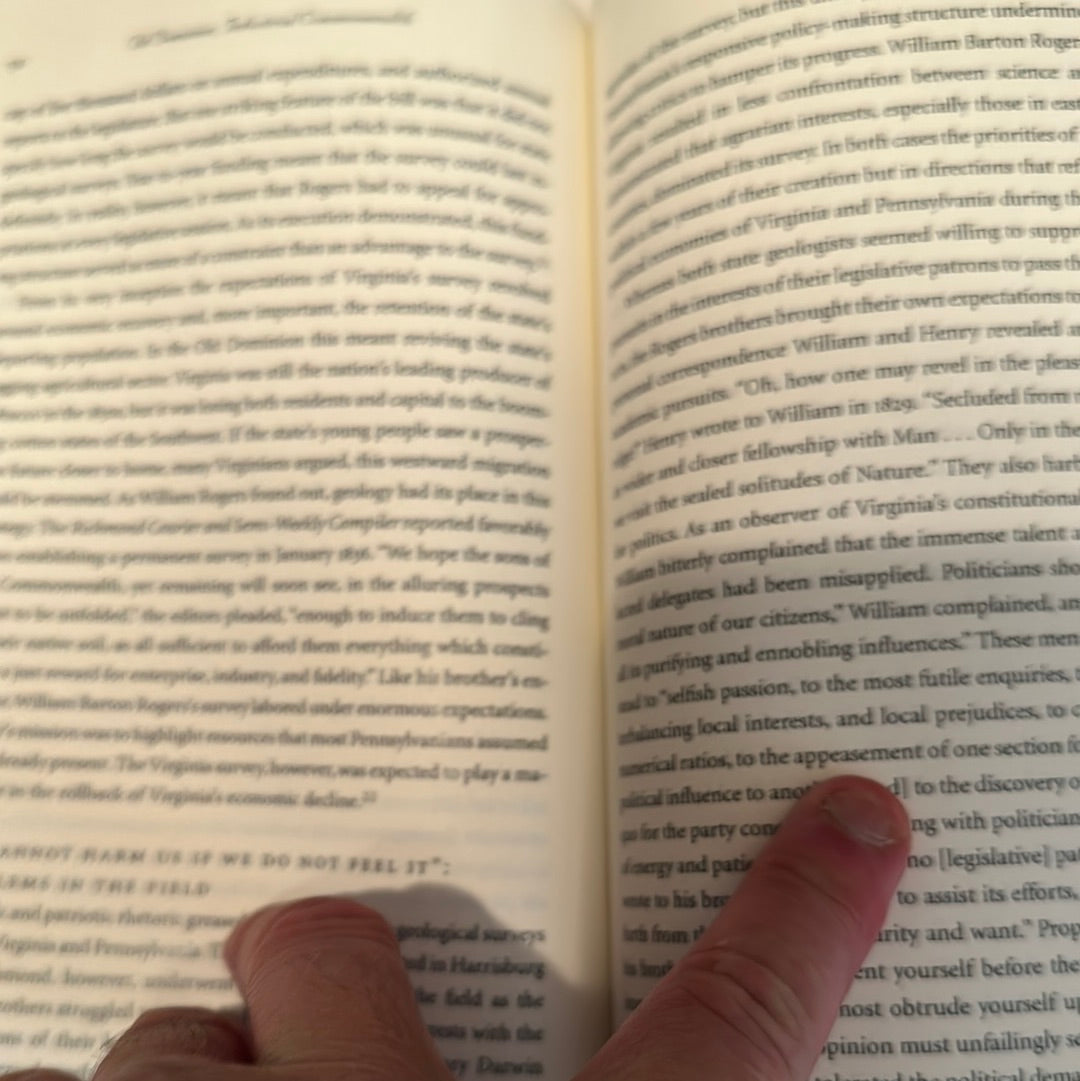 Close-up of a person holding and pointing to text in the Old Dominion Industrial Commonwealth book