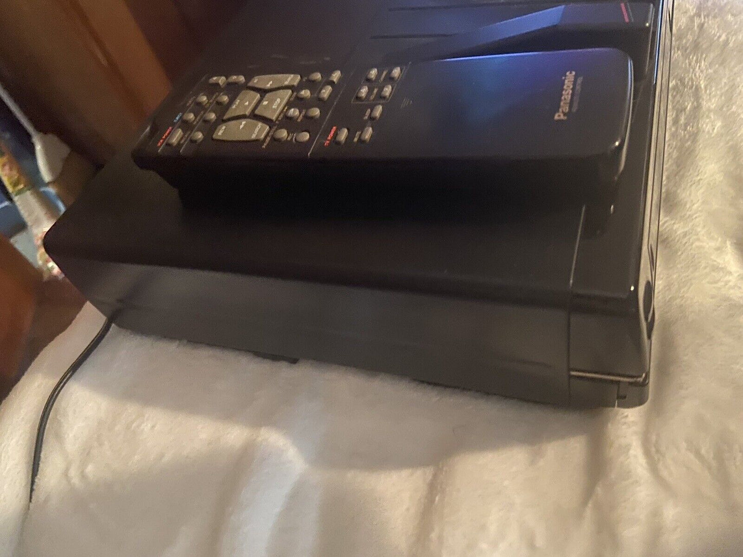 Panasonic OmniVision VHS player black vintage VCR with remote control on top resting on white blanket